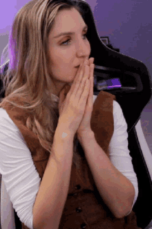 a woman covering her mouth with her hands while wearing a brown vest