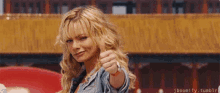 a blonde woman is pointing at the camera while wearing a denim jacket .