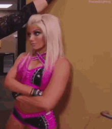 a woman in a pink outfit is standing with her arms crossed and looking at the camera .