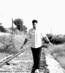 a man is walking on train tracks in a black and white photo .