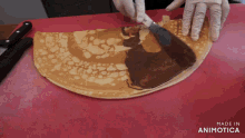 a person is spreading chocolate on a crepe and the words made in animotica can be seen behind them