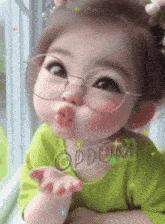 a little girl wearing glasses and a green shirt is blowing a kiss ..