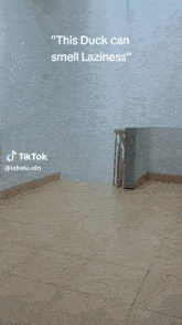 a blue duck mascot is standing on a tiled floor with the caption " this duck can smell laziness " above it