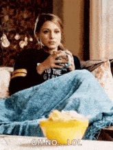 a woman is sitting on a couch holding a cup of coffee and eating popcorn .