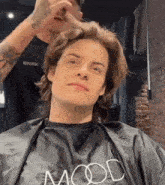 a man is getting his hair cut by a man wearing a black cape that says mood