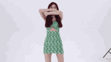 a woman in a green dress is standing in front of a white wall .