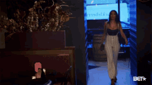 a woman in a black top and striped pants is walking into a room with a sign that says bet