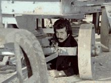 a man with a mustache is hiding under a wheel