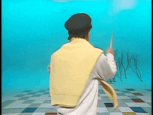 a man wearing a yellow vest and a black hat is standing on a checkered floor holding a piece of paper .