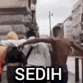 a group of people are walking down a street with the word sedih on the sidewalk .