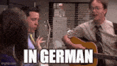 a man is playing a guitar in front of a group of people and the caption says in german .