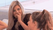 two women are sitting on a couch and one is covering her nose