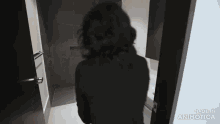a woman in a black shirt is standing in a bathroom looking out the door .