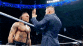 a man in a suit gives another man a high five in a wrestling ring