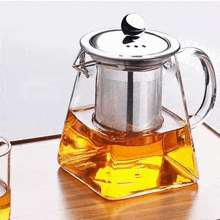 a glass teapot with a stainless steel filter is sitting on a wooden tray next to a glass of tea .