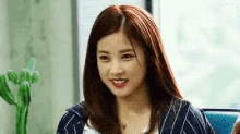 a woman with red hair is smiling and looking at the camera while sitting in front of a window .