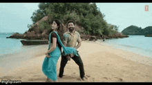 a man and a woman are dancing on a beach . the woman is wearing a blue saree .
