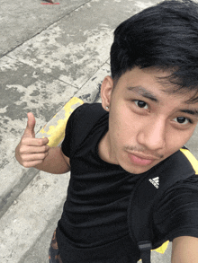a man wearing a black adidas shirt is giving a thumbs up