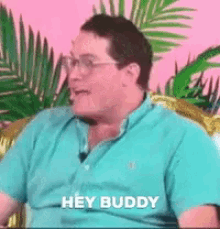 a man wearing glasses and a blue shirt is sitting on a couch and says hey buddy .