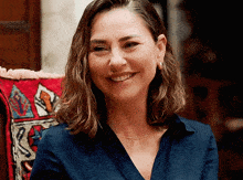 a woman wearing a blue shirt and earrings smiles