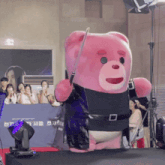 a pink teddy bear holding a sword stands in front of a sign that says ' a ' on it