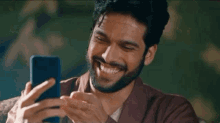 a man with a beard is smiling while taking a selfie with his cell phone .