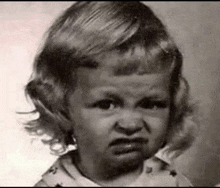 a black and white photo of a little girl with a very angry look on her face .