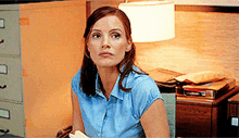 a woman in a blue shirt sits in front of a lamp