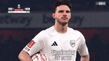 a soccer player wearing an emirates fly better jersey holds a soccer ball
