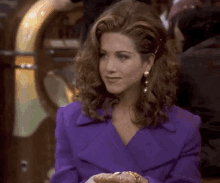 a woman in a purple jacket and earrings is sitting in front of a jukebox and looking at the camera .