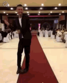 a man in a suit is dancing on a red carpet in a large room