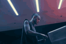 a man in a black tank top is standing in a dark room with a red light behind him