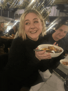 a woman is smiling while holding a plate of food in front of a sign that says bf