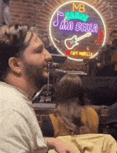 a man is sitting in front of a neon sign that says mia bella .