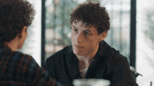 two young men are sitting at a table talking to each other