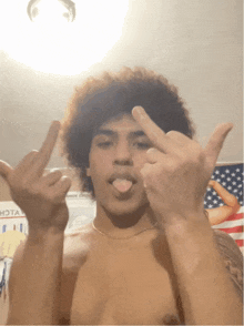 a shirtless man giving the middle finger with his tongue out in front of an american flag