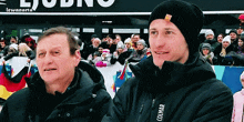 a man in a colmar jacket stands next to another man