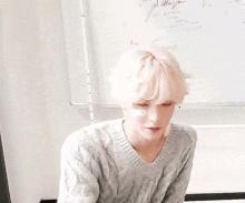 a young man with white hair is sitting in front of a white board .
