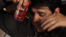 a man is drinking from a can of soda while sitting on a bed .