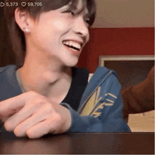 a young man wearing a blue hoodie is sitting at a table laughing .