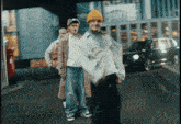 a man wearing a yellow beanie is walking down the street with two other men