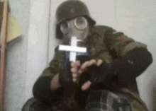 a man wearing a gas mask is holding a cross in his hands .