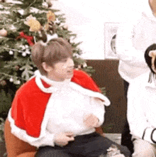 a man in a santa costume is sitting in a chair in front of a christmas tree .