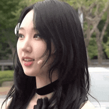 a woman with long black hair is wearing a choker and a microphone .