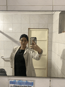 a woman taking a selfie in front of a sign that says please keep this sink