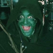 a person with green paint on their face is wearing glasses and a hoodie