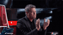 a man applauds while sitting in front of a chair that says nbc on it