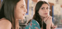 two women are sitting next to each other at a table and talking .