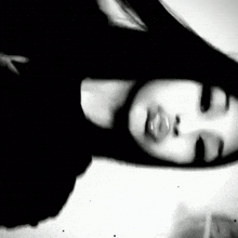 a black and white photo of a woman with her eyes closed and her hair blowing in the wind .