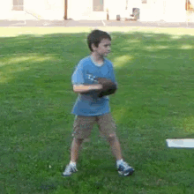 a young boy in a blue shirt is holding a baseball glove while standing in the grass .